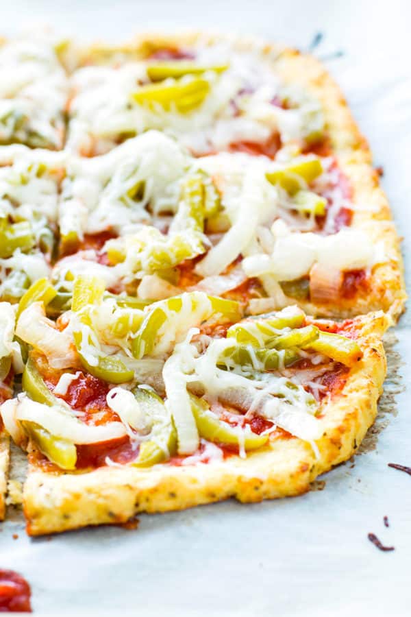 Half of a cauliflower pizza crust recipe topped with fresh vegetables for a healthy lunch.