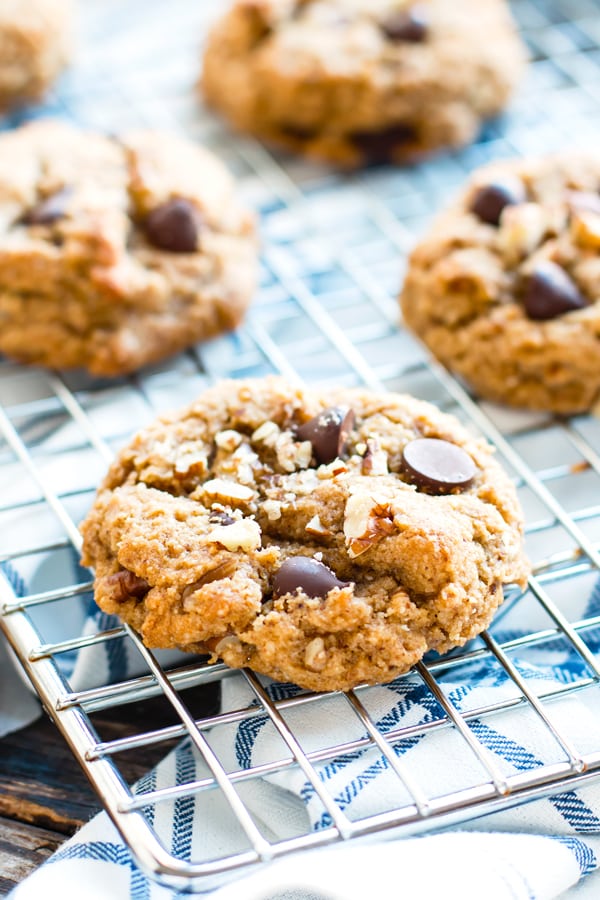 Soft chocolate chip cookies with pecans on a cooling rack with a napkin underneath.
