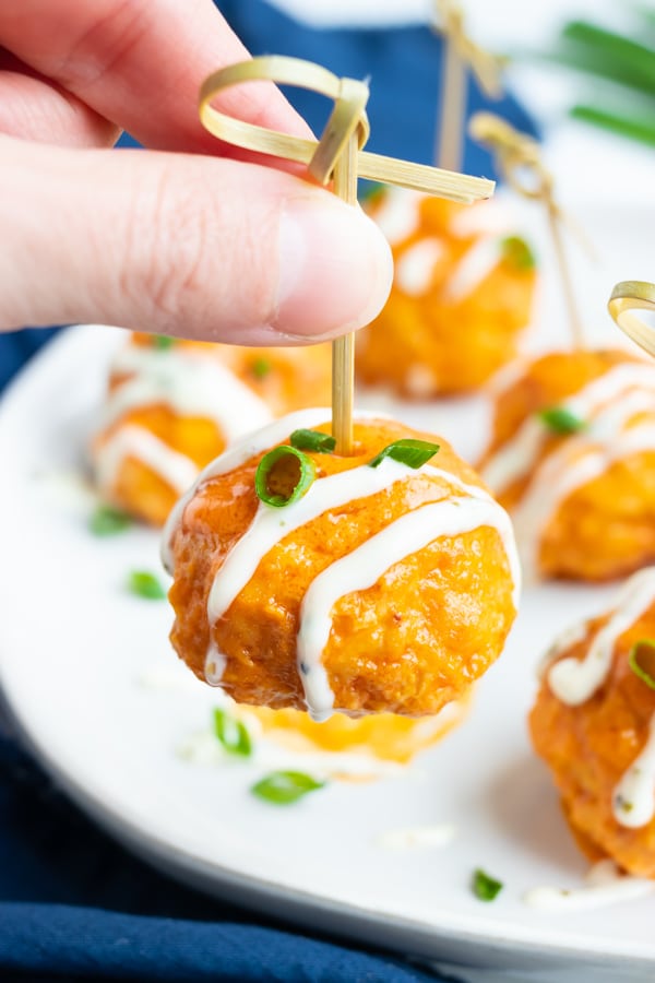 A hand picking up a slow cooker buffalo chicken meatball from a party tray.
