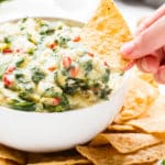Vegan spinach dip made with artichokes being scooped up with a tortilla chip.