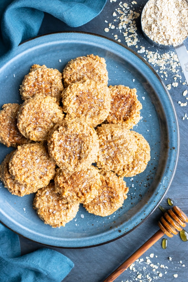 Almond butter cookies on a blue plate next to honey and oats.