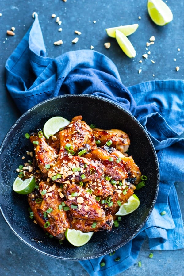 Healthy gluten-free chicken wings with Thai sauce in a black bowl on a blue table.