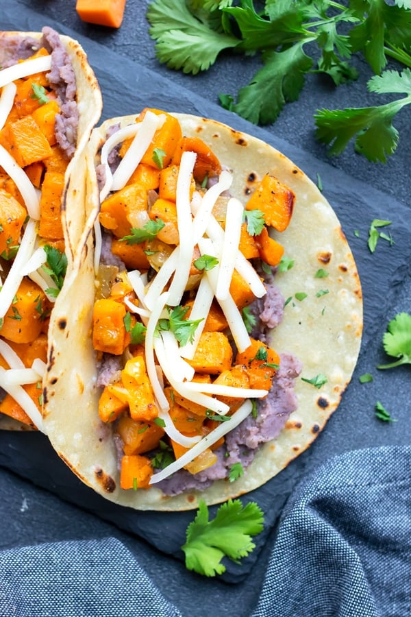 A corn tortilla full of sweet potatoes, beans, cheese, and topped with cilantro.