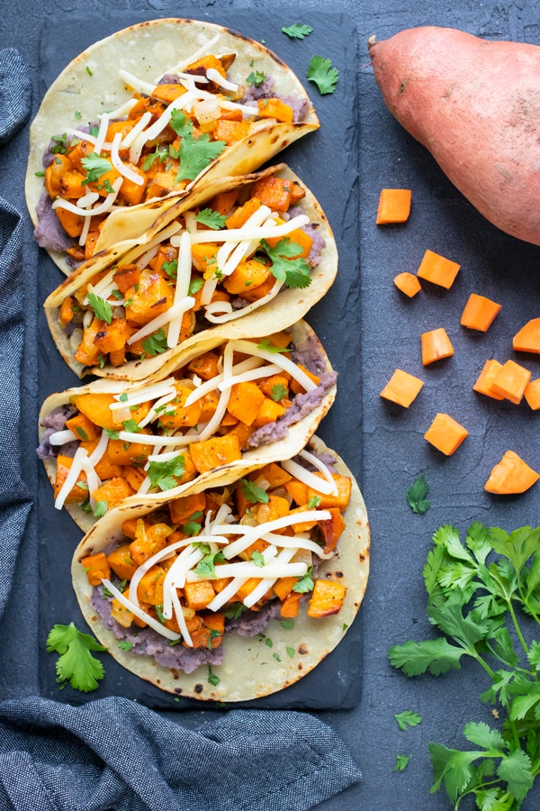 Four healthy and vegetarian tacos with refried beans and cubed sweet potatoes.