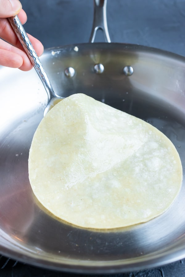 A corn tortilla being lightly toasted in coconut oil in a skillet for a taco.