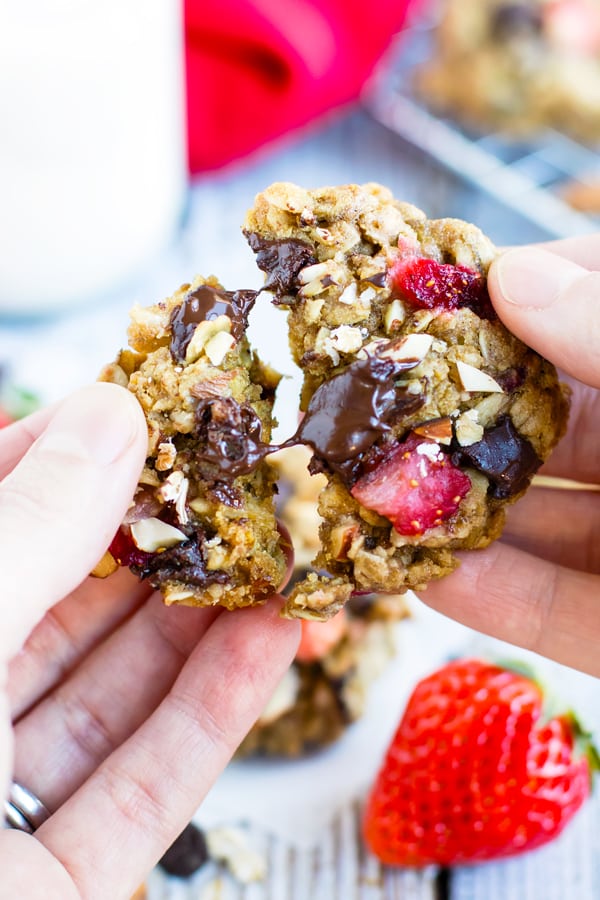 A hand pulling apart one Strawberry Chocolate Chip Oatmeal Cookie.