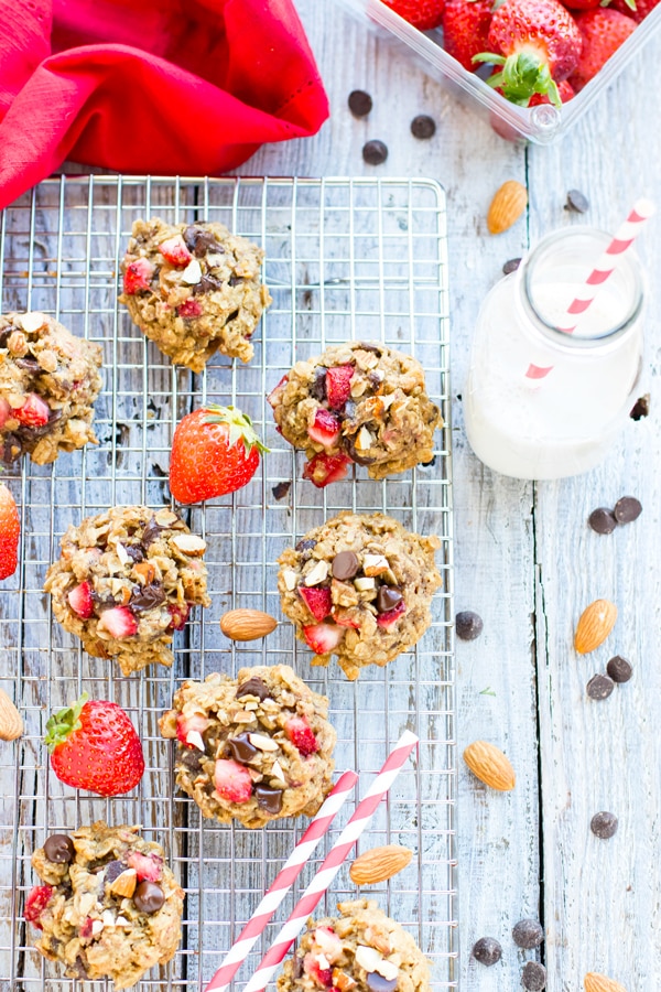 Gluten-free oatmeal chocolate chip cookies with strawberries on a cooling rack with a glass of milk.