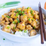 Healthy orange chicken with green onions and chopsticks in a white dinner bowl.