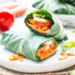 Two hummus veggie wraps on a plate with tomatoes in the background.