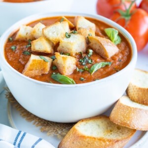 A soup bowl full of creamy roasted tomato basil soup with homemade croutons.