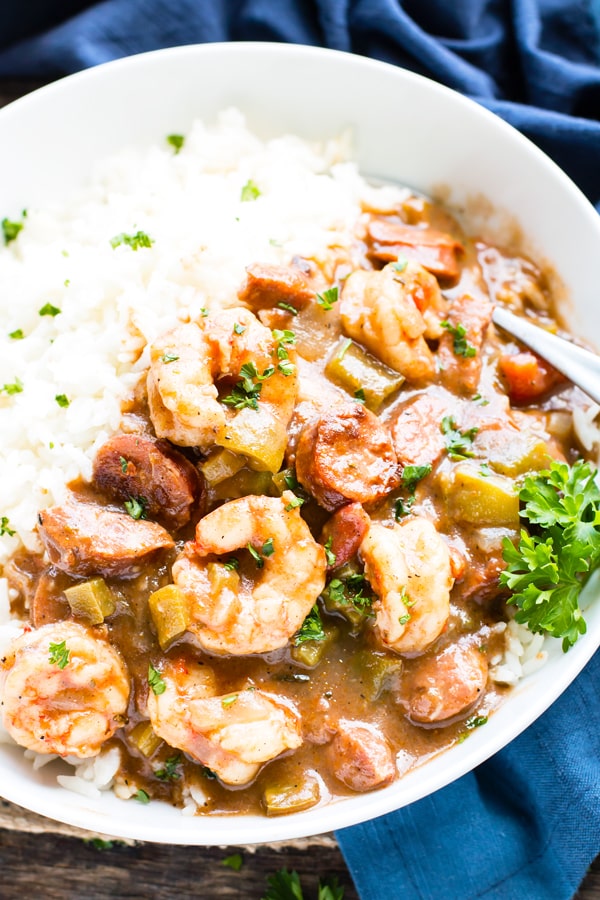 A bowl full of shrimp and sausage gumbo with a sprig of parsley.