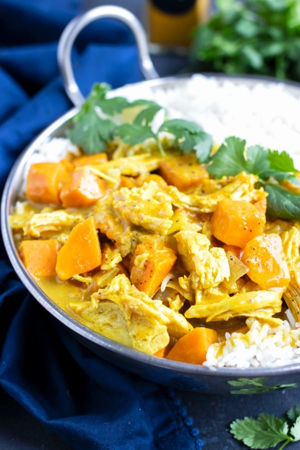 A close view of shredded chicken breasts in a yellow curry sauce with big chunks of sweet potatoes.