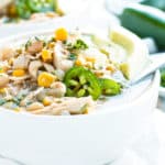 A spoon resting in a bowl of crockpot white chicken chili with a lime wedge and jalapeños.