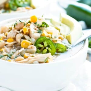 A spoon resting in a bowl of crockpot white chicken chili with a lime wedge and jalapeños.