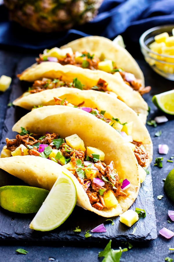 A delicious row of Pork al pastor tacos with fresh pineapple and spicy chipotle.