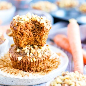 Two carrot cake muffins piled on a plate with a bite taken out.