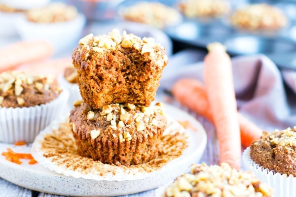 Two carrot cake muffins piled on a plate with a bite taken out.