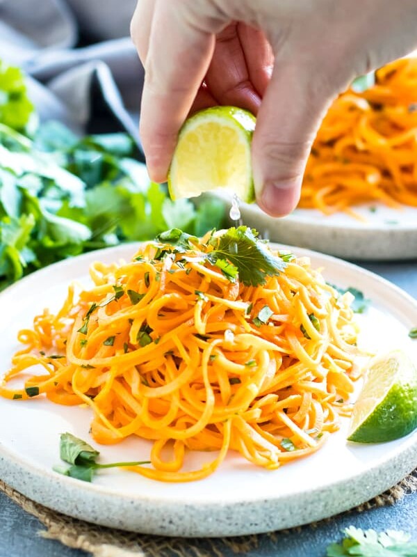 A hand squeezing the juice of a lime onto Cilantro Lime Sweet Potato Noodles.