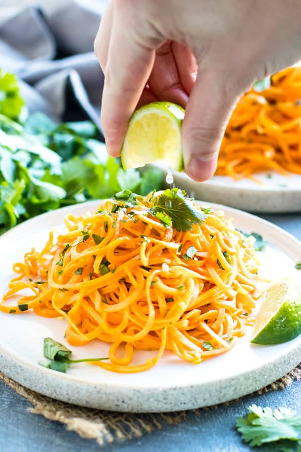A hand squeezing the juice of a lime onto Cilantro Lime Sweet Potato Noodles.