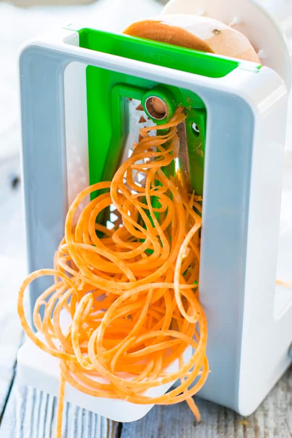 A picture of a sweet potato going through a spiralizer to create sweet potato noodles.