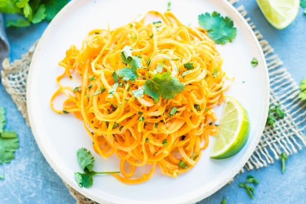 Gluten-free sweet potato noodles on a white plate with a lime on the side.