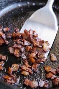Cooking Paleo, Whole30, and keto bacon pieces in a cast iron skillet.