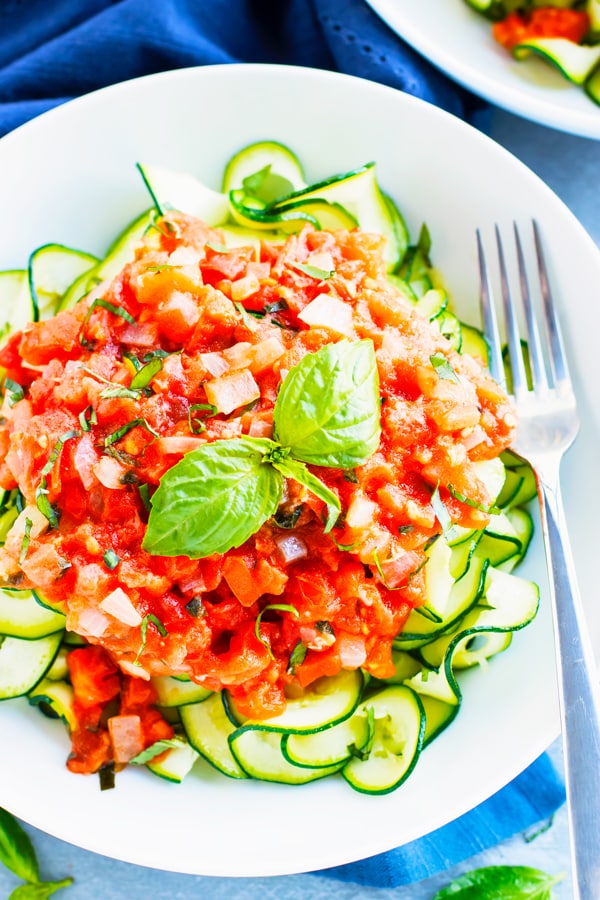 Tomato basil zucchini noodles in a white bowl for a healthy dinner.