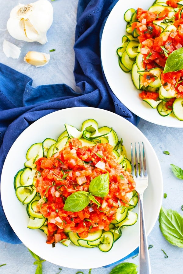Two bowls of gluten-free tomato basil zucchini noodles with a blue napkin.
