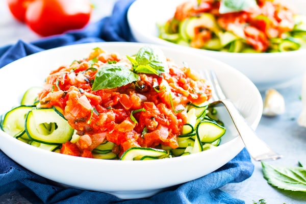 A bowl of healthy zucchini noodles topped with fresh tomato basil.
