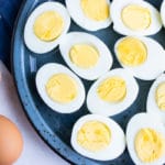 A blue plate full of hard-boiled eggs that are cut in half.