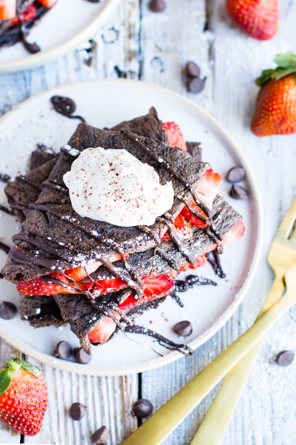 Gluten-free chocolate crepes with strawberries surrounded by chocolate chips.