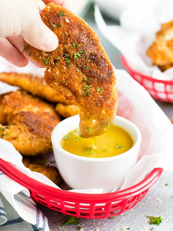 One gluten-free and paleo fried chicken tender being dipped in honey mustard sauce for lunch.