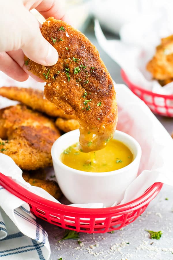 One gluten-free and paleo fried chicken tender being dipped in honey mustard sauce for lunch.