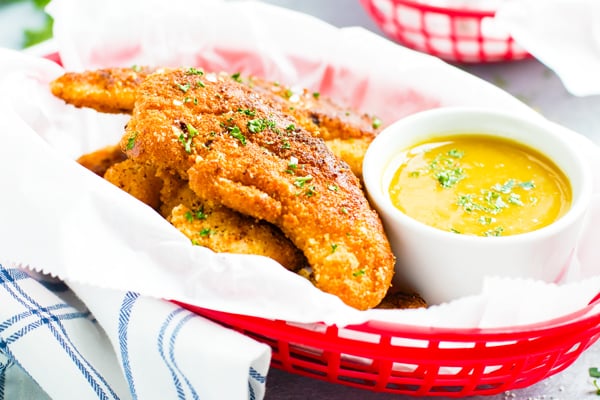 Paleo fried chicken tender recipe in a red basket with honey mustard sauce.