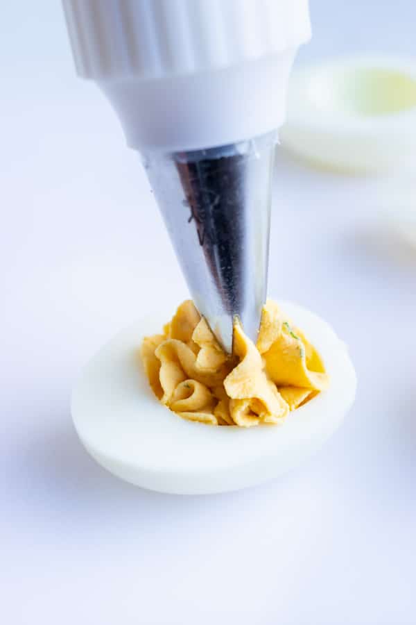 A piping bag with a large tip piping a creamy yellow yolk filling into a hard-boiled egg white.