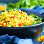 Paleo cauliflower rice in a black bowl with seasonings on the side.