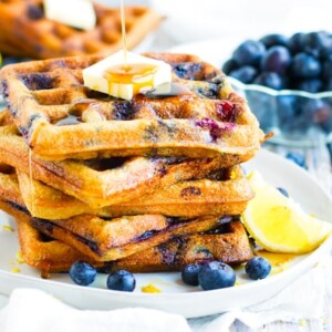 A stack of paleo waffles with blueberries on a plate.