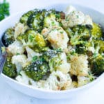 Serve roasted broccoli cauliflower in a bowl topped with fresh parsley for a keto side dish.