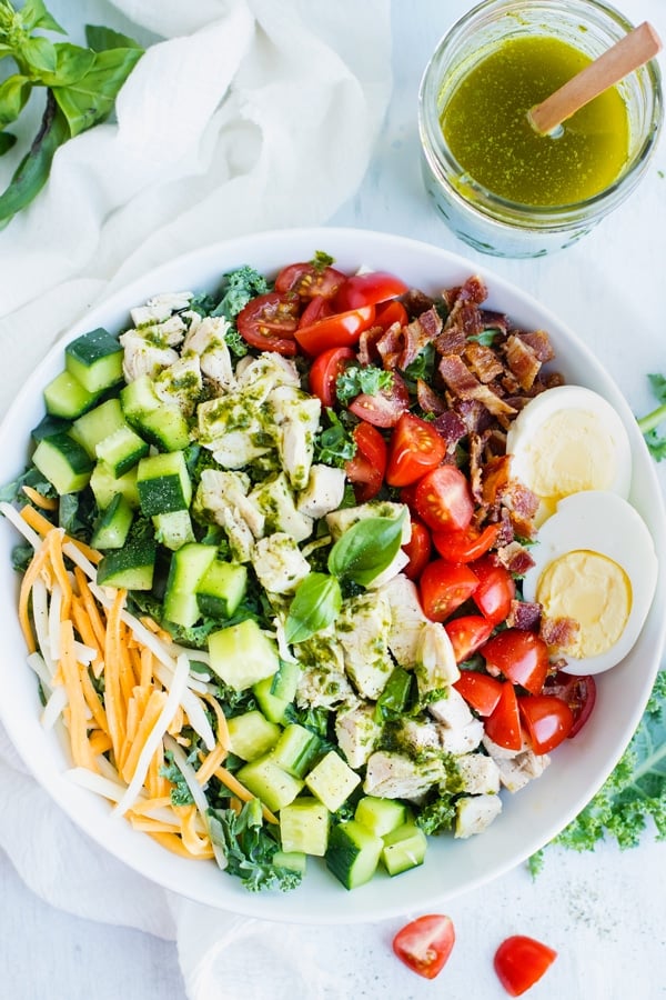 Chicken Cobb Chopped Kale Salad in a white bowl with a drink on the side.