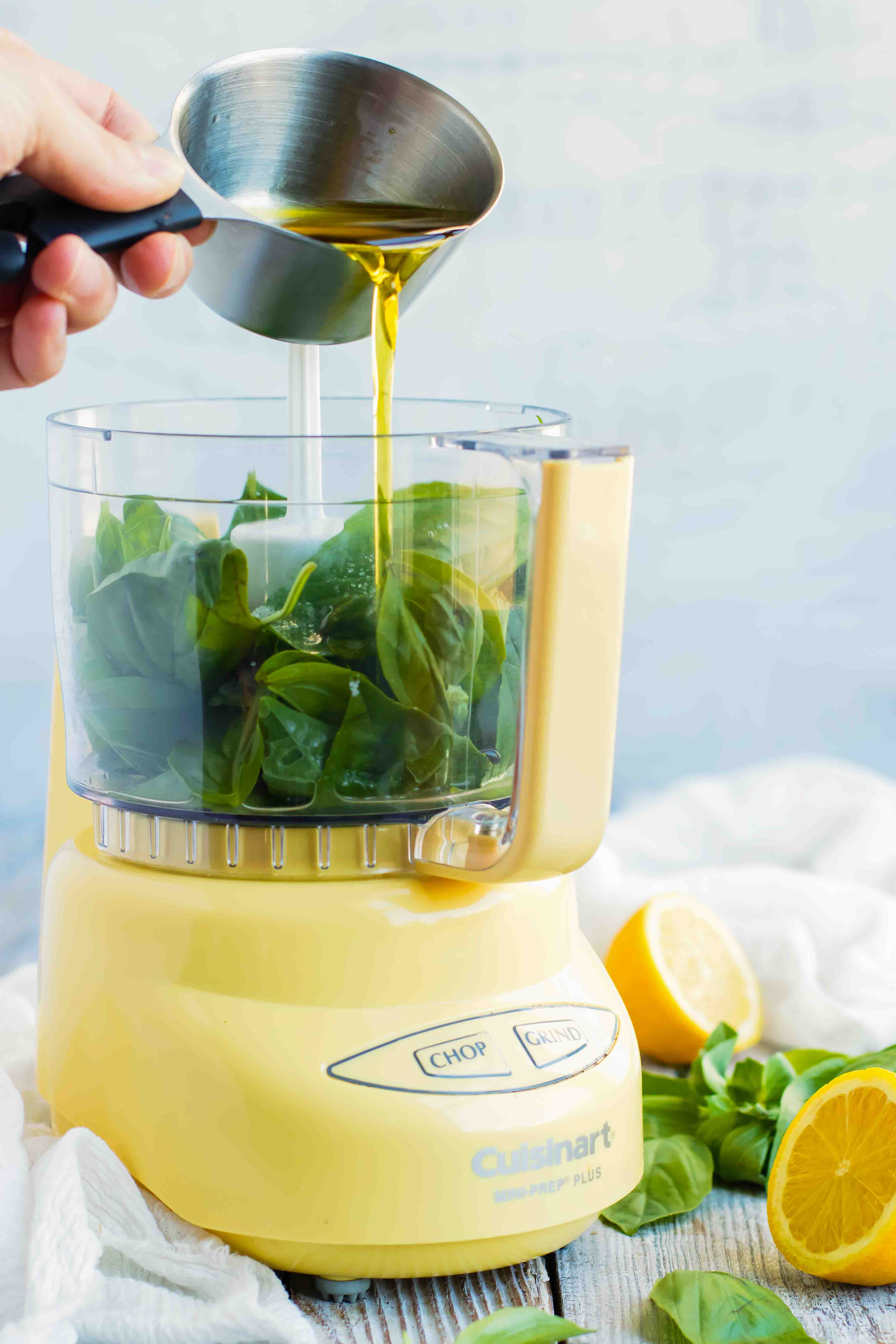 Lemon vinaigrette poured into a food processor with basil leaves inside.