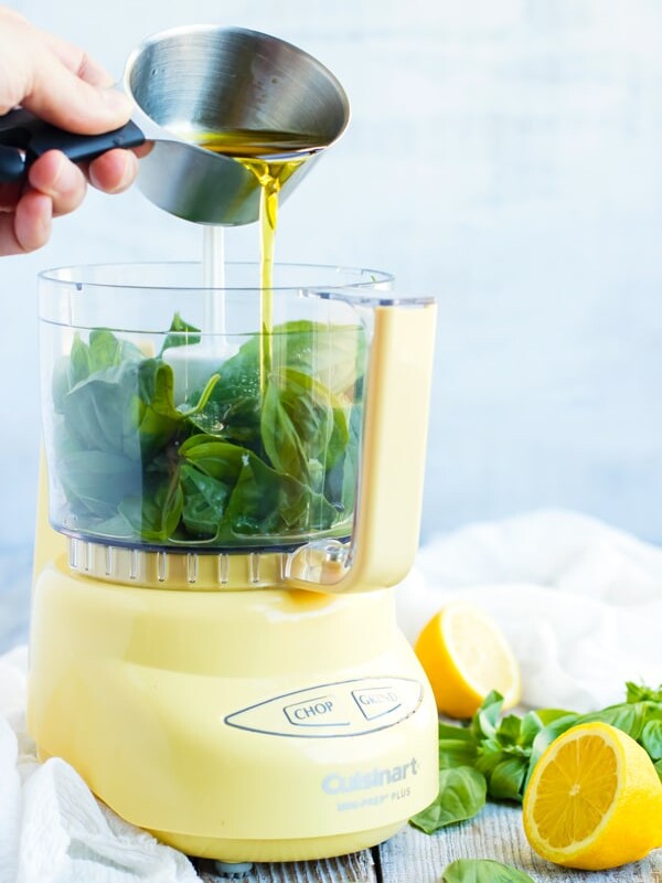 Lemon vinaigrette poured into a food processor with basil leaves inside.