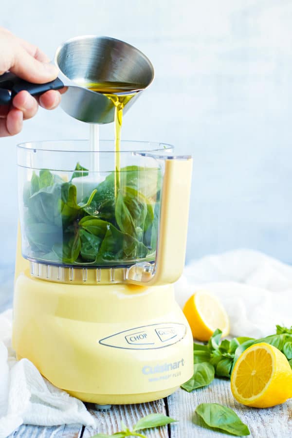 Lemon vinaigrette poured into a food processor with basil leaves inside.