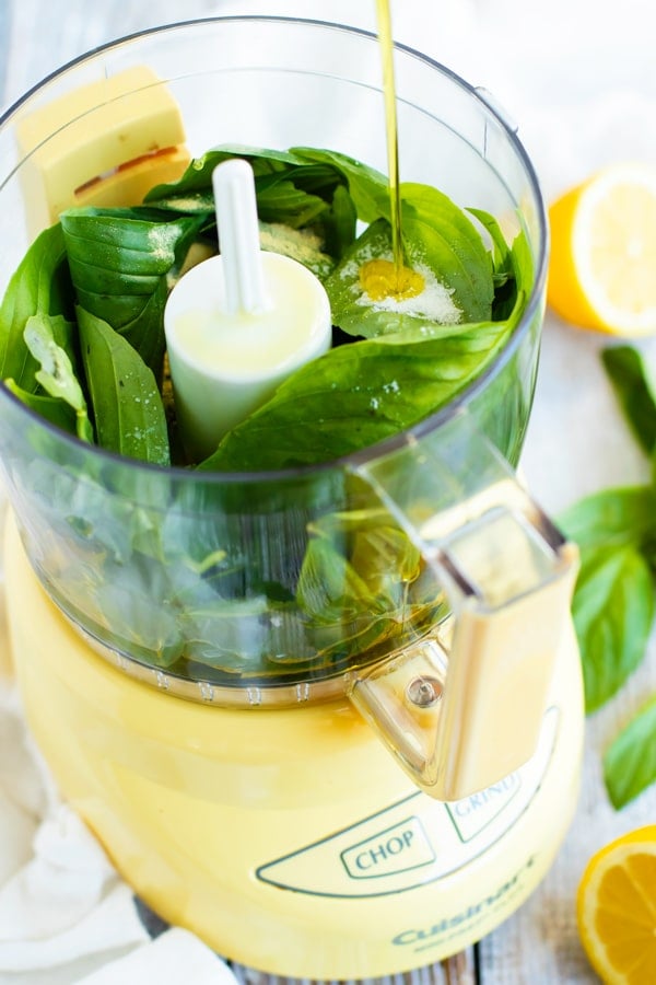 Basil with lemon vinaigrette poured into a food processor.