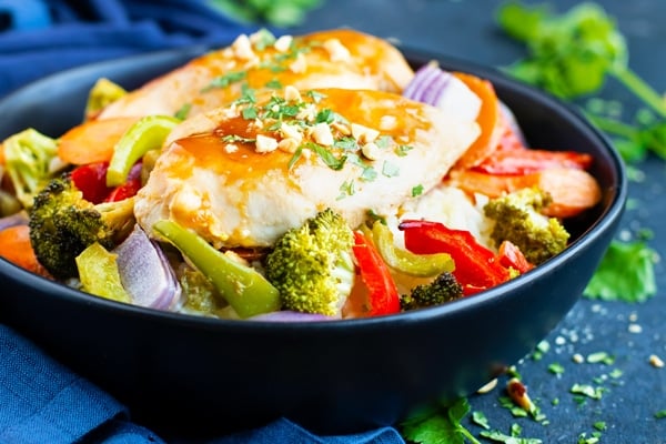 Peanut sauce chicken recipe in a black bowl surrounded by vegetables.