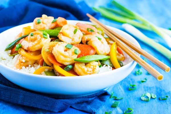 Shrimp and vegetable stir fry in a white bowl with chopsticks.