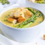 Non-dairy, healthy, vegetarian asparagus soup recipe in a white bowl next to toasted bread.