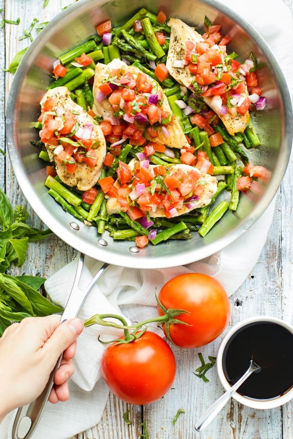 Beautiful overhead picture of Skillet Bruschetta Chicken and Asparagus in a silver skillet with whole tomatoes.