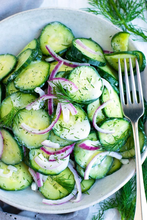 A bowl filled with healthy, gluten-free cucumber dill salad with a fork on the side.