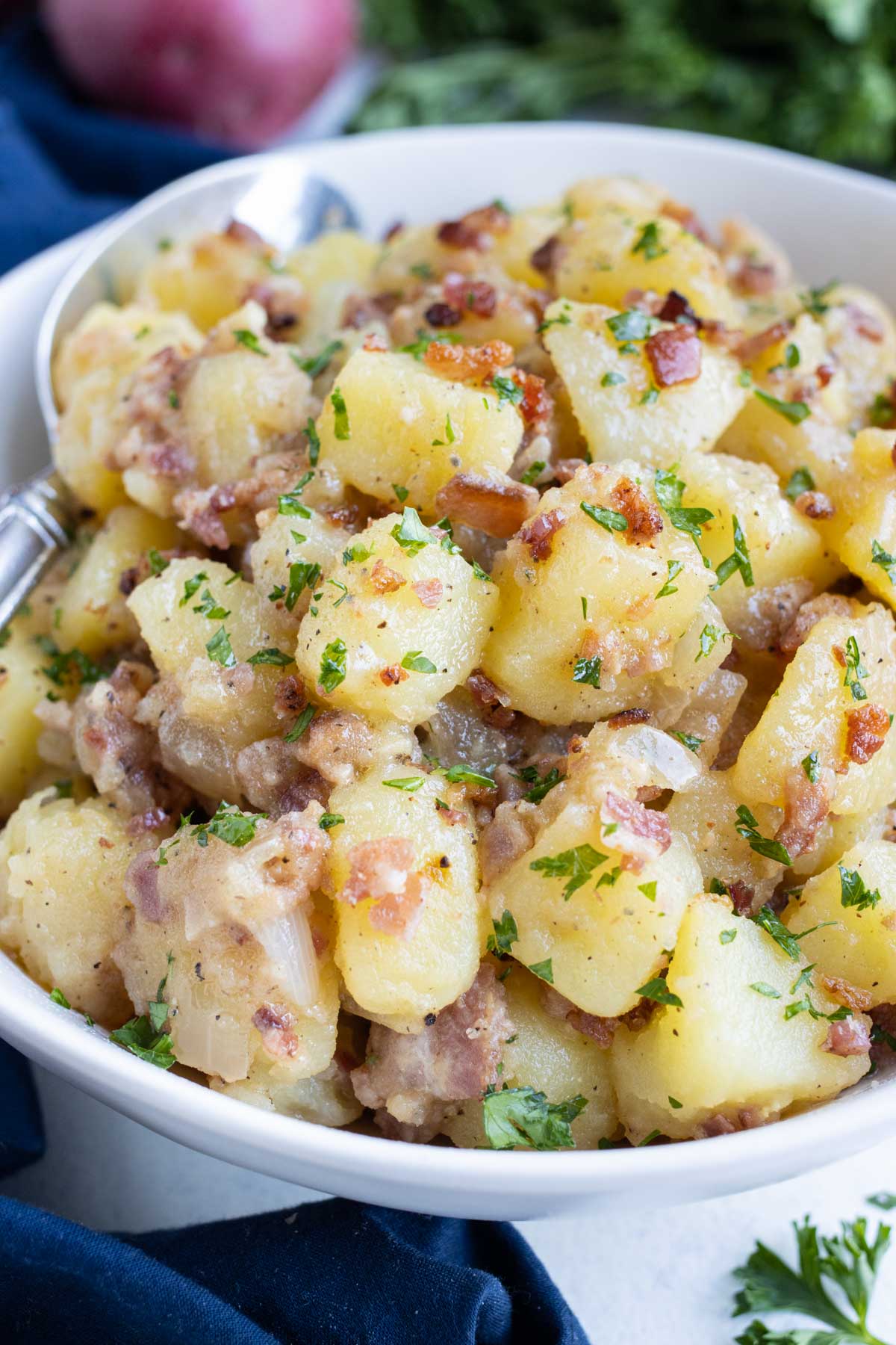 Old-Fashioned German Potato Salad RECIPE served in a white bowl with a spoon.