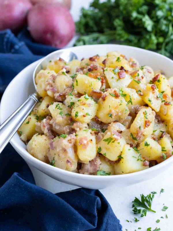 A white bowl is filled with authentic German potato salad for a delicious side dish.
